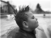 Black and white photo of a boy in a pool with a mohawk. 