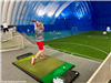 A boy teeing off at an indoor golf facility. 