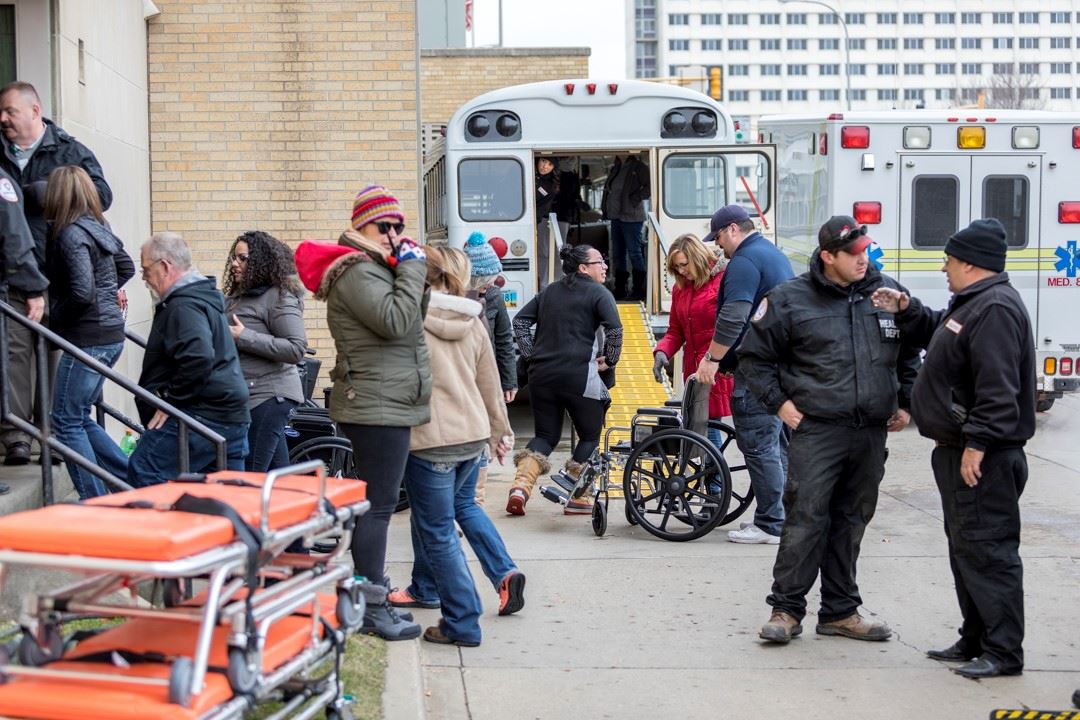 Woman holding radio standing in front of ambulance, wheelchairs and strechers used to evacuate.