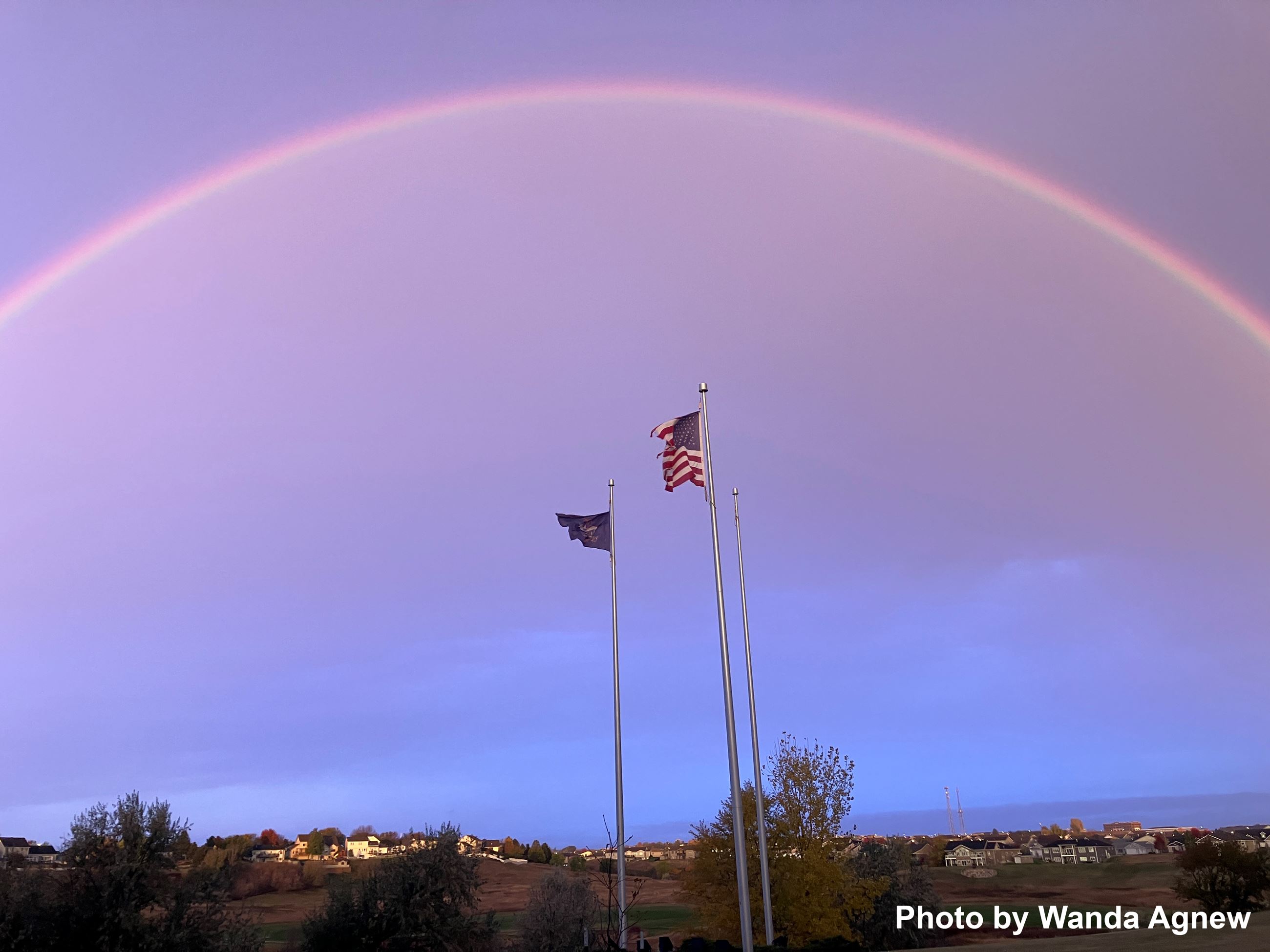 Rainbow appearing over flags on flagpoles. 