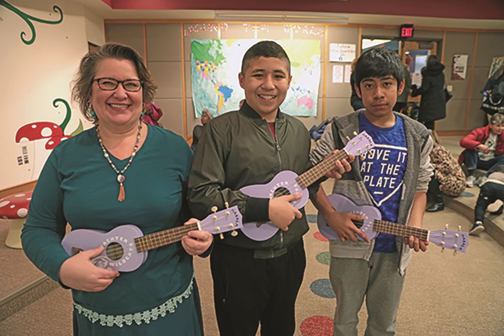 Two students and a teacher holding ukeleles
