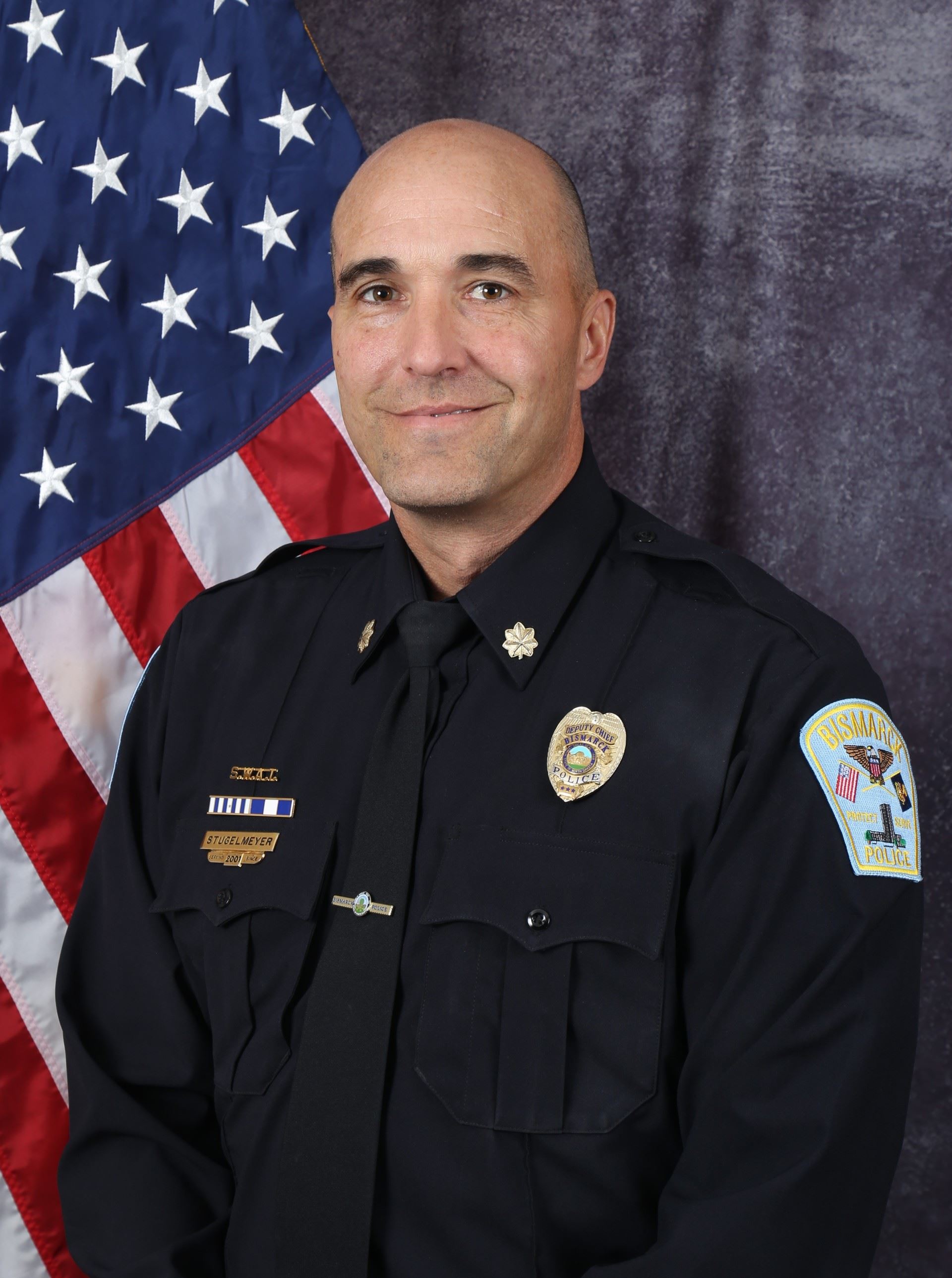 Man wearing a police uniform in front of an American flag. 