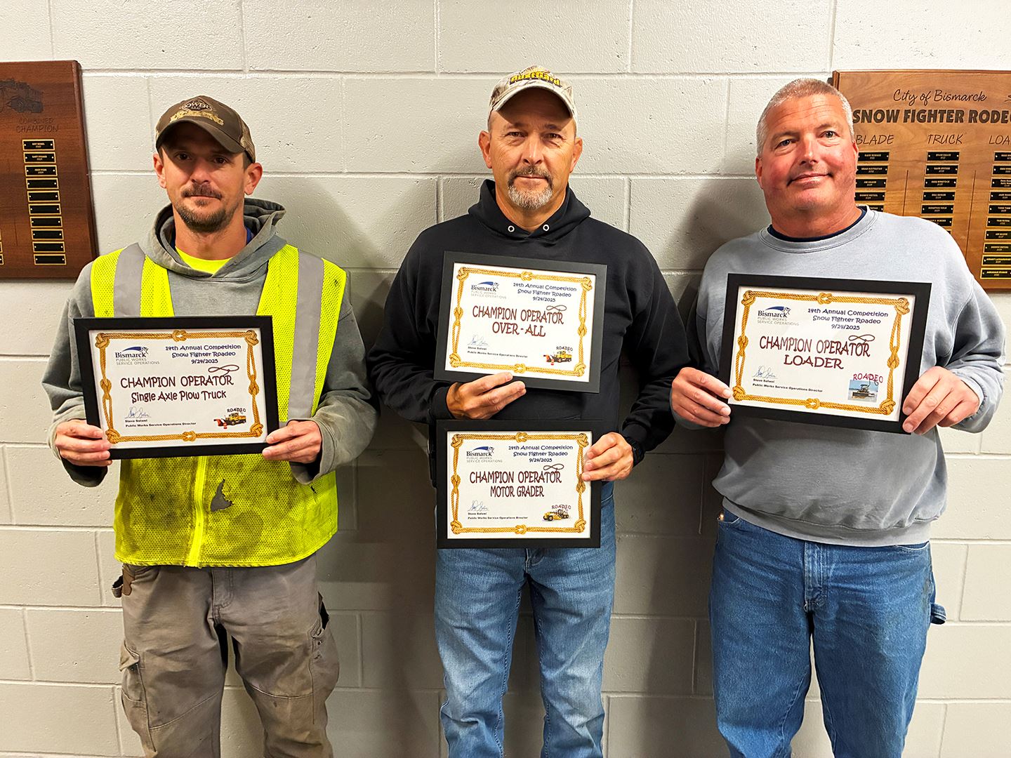 Three men standing against a wall holding certificates. 